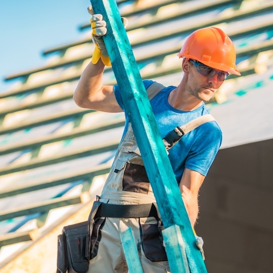 A roofer is lifting a heavy pole whilst roofing.